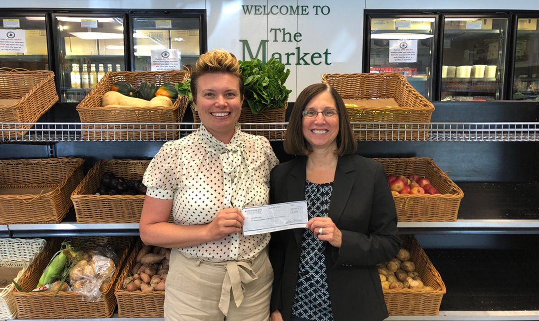 Photo of Lyndsey Haight, Executive Director of Our Neighbors' Table receiving a $1,400 donation from Deb Alphonse of North Shore Bank.
